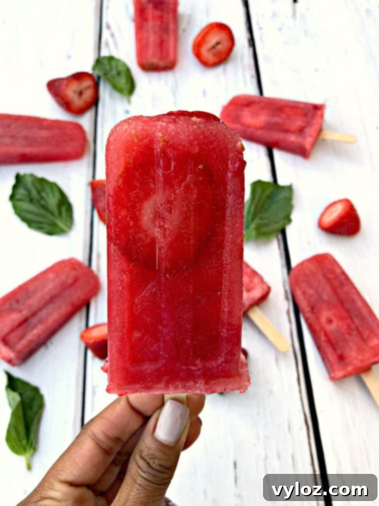 Three Rosé wine popsicles with basil and strawberries, vibrant and refreshing, on a dark background.