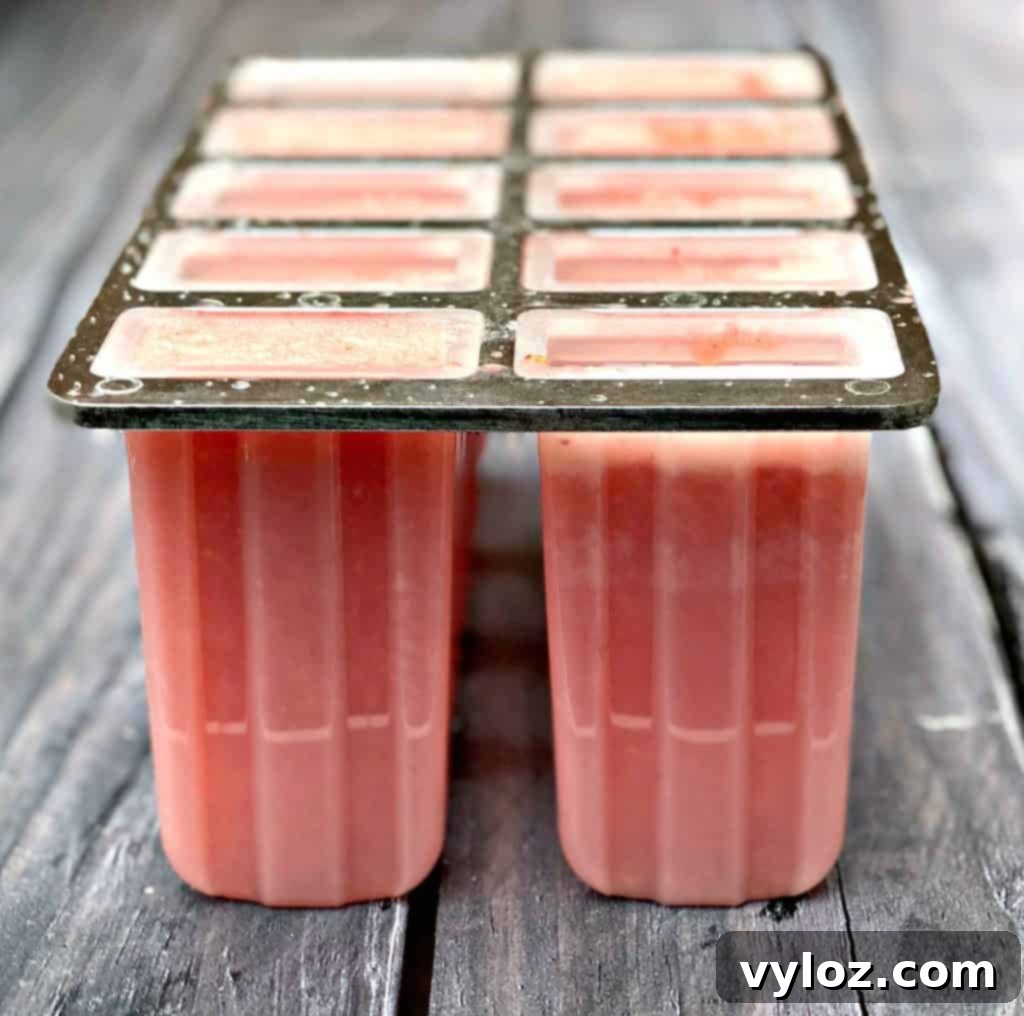 Rosé wine popsicle mixture carefully poured into a mold, with strawberry slices added for garnish.