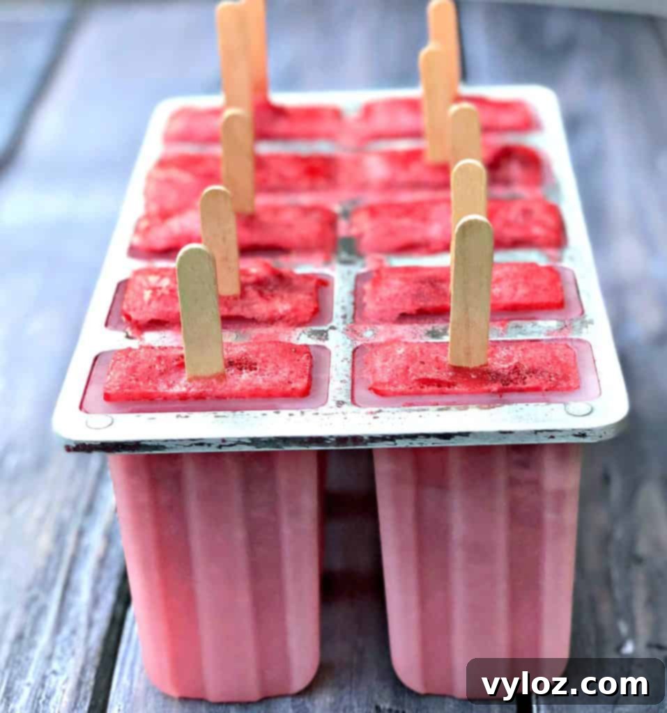 A tray of Rosé wine popsicles, partially frozen in their mold, with popsicle sticks just inserted.