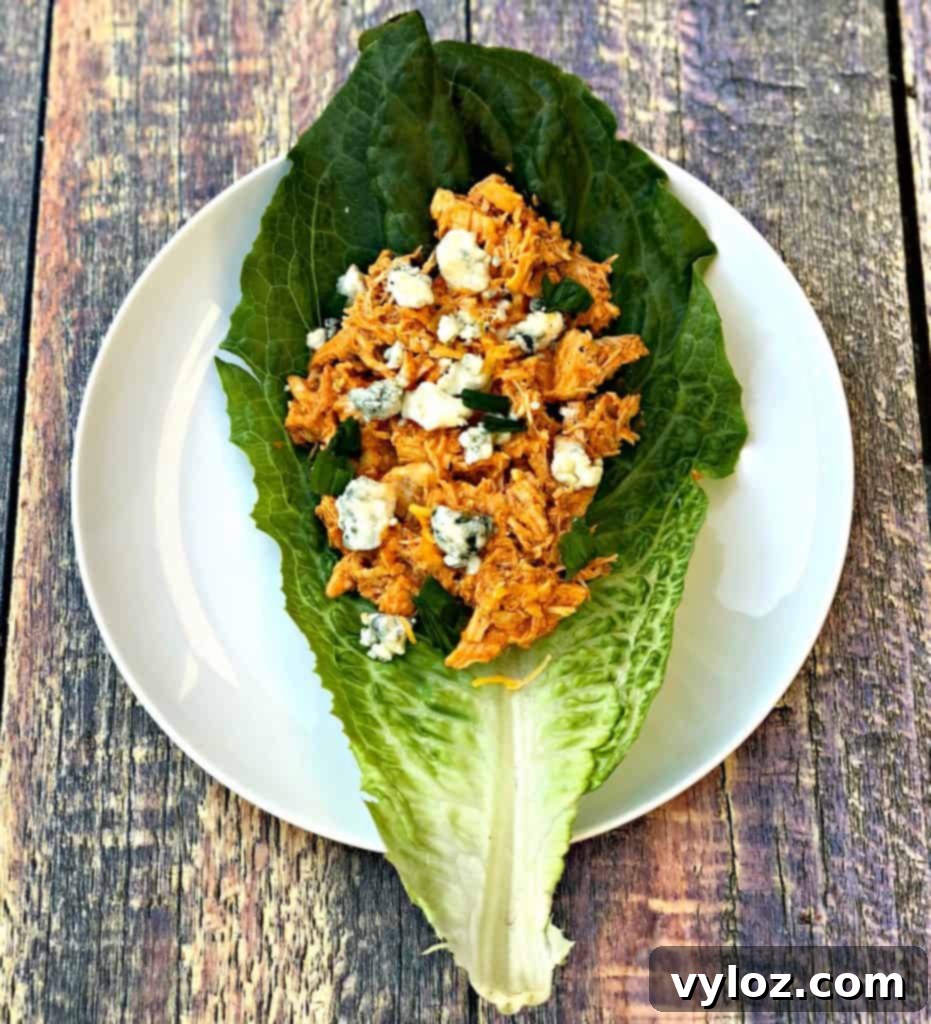 Spicy Cheesy Instant Pot Keto Buffalo Chicken Lettuce Wraps 2 Crisp romaine lettuce wraps filled with cheesy buffalo chicken, garnished with blue cheese crumbles and green onions, presented on a wooden cutting board.
