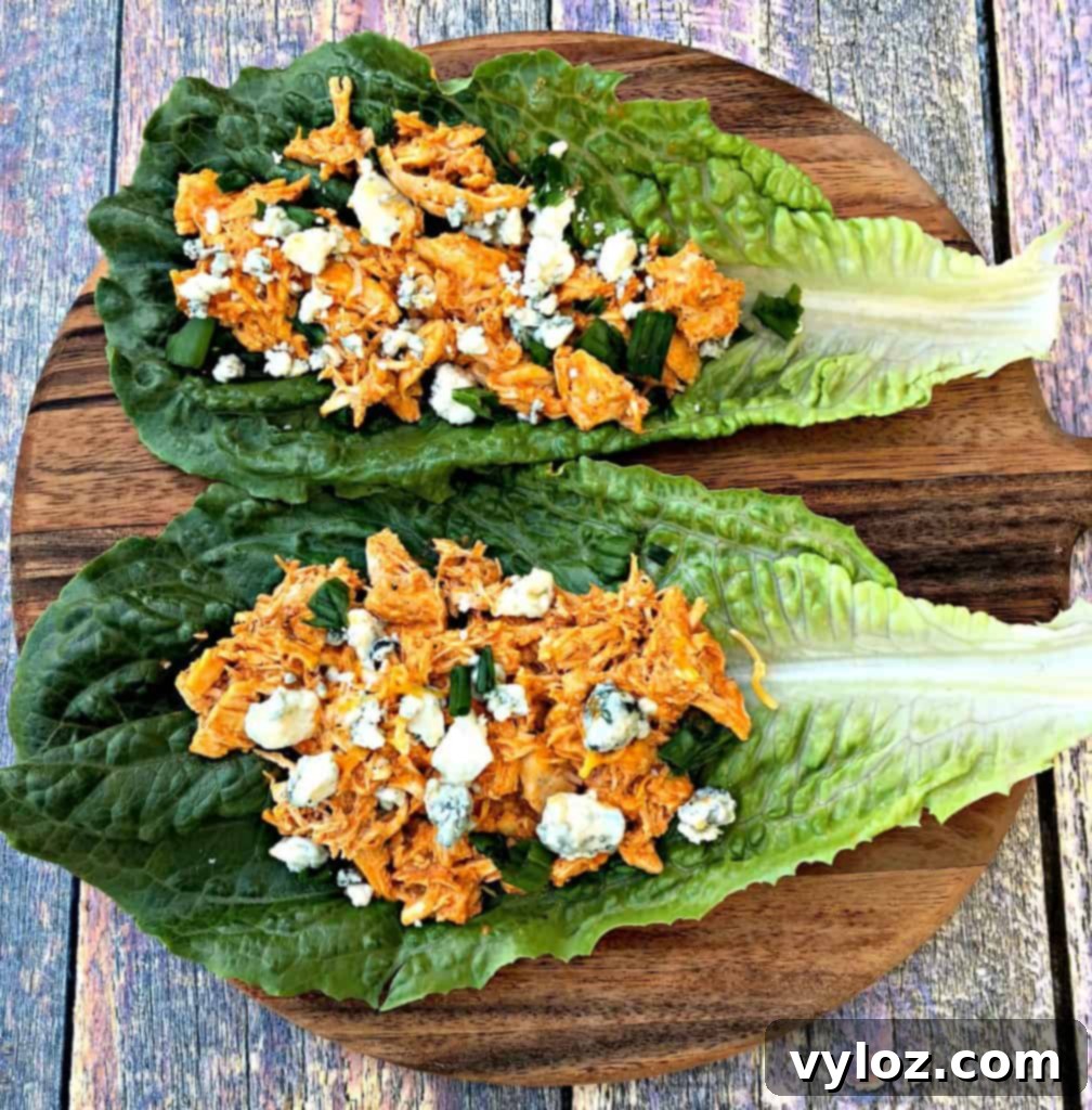 Spicy Cheesy Instant Pot Keto Buffalo Chicken Lettuce Wraps 3 Close-up of a buffalo chicken lettuce wrap, showcasing the shredded chicken, melted cheese, and fresh garnishes against a rustic backdrop.