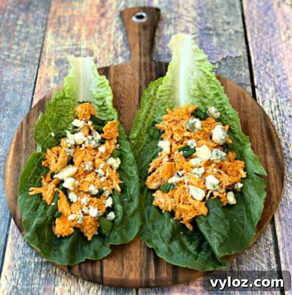 Spicy Cheesy Instant Pot Keto Buffalo Chicken Lettuce Wraps 6 A close-up view of a buffalo chicken lettuce wrap, beautifully garnished with blue cheese crumbles, on a wooden board.