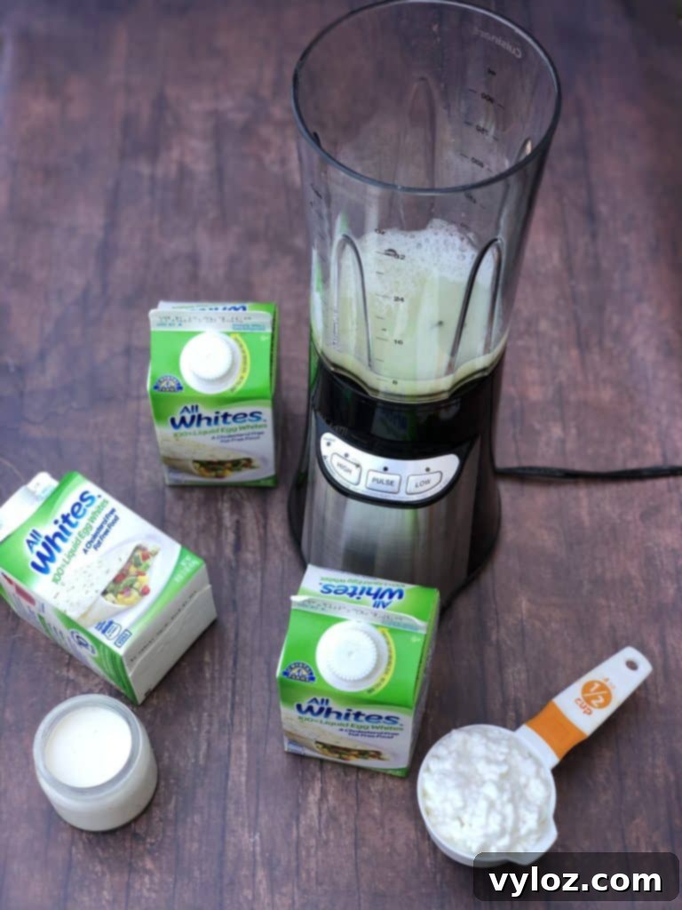 Keto Veggie Egg White Bites 4 Liquid egg whites in a blender, alongside a bowl of whipping cream and cottage cheese, ready to be blended for a smooth egg bite mixture.