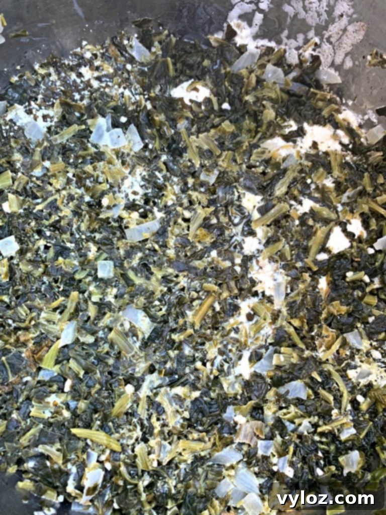 Simple Keto Creamy Garlic Spinach 4 Creamed spinach cooking in a pan, with a wooden spoon stirring the creamy mixture.