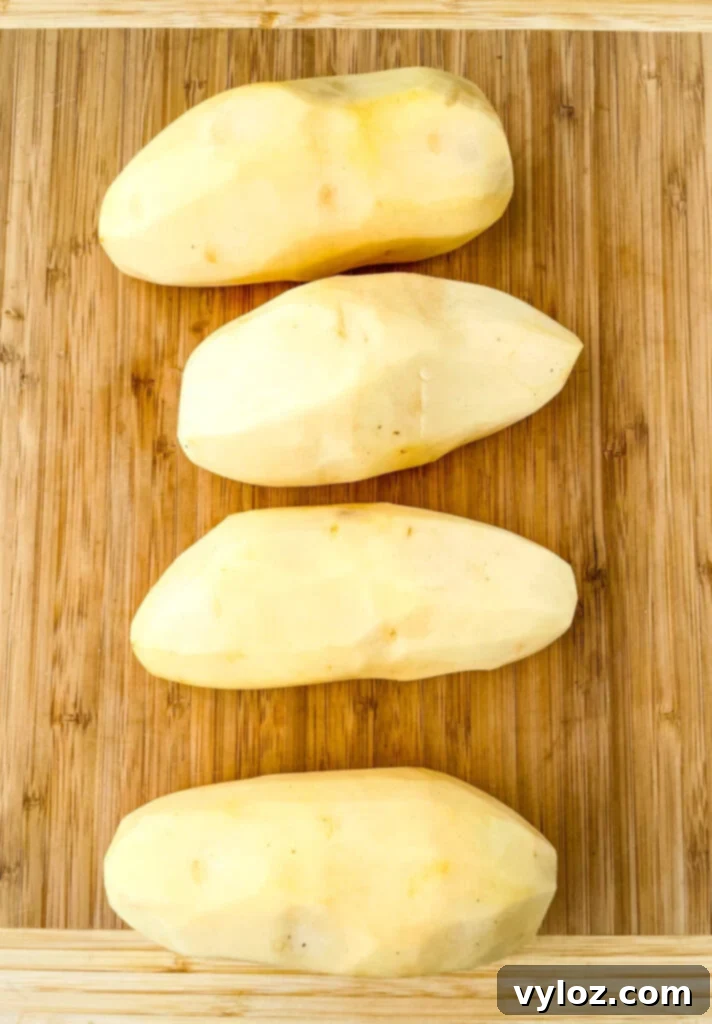 raw russet potatoes peeled on a bamboo cutting board