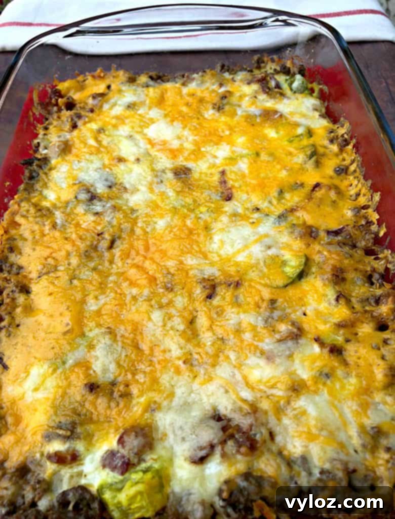 Keto Cheeseburger Bake 11 A whole Keto Cheeseburger Casserole in a rustic baking dish, with a golden-brown, bubbly cheese topping, resting on a wooden surface, ready to be sliced.