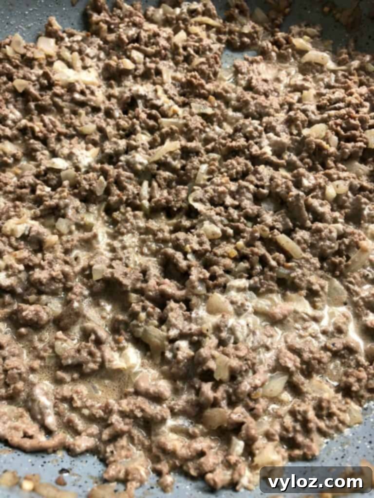 Keto Cheeseburger Bake 5 A large baking dish filled with a creamy, cheesy keto cheeseburger casserole, topped with melted cheddar and garnished with fresh green onions and crispy bacon bits.