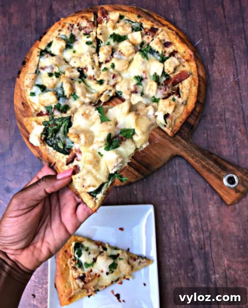Indulgent Keto Chicken Alfredo Pizza 9 person holding slice of keto fathead alfredo bacon chicken pizza on a pan