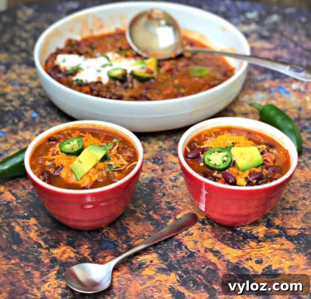 Assorted toppings for chili, including shredded cheese, diced onions, and sour cream, beside a bowl of chili.