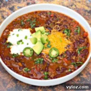 instant pot chili with shredded cheese, avocado, sour cream and jalapeno served in a white bowl