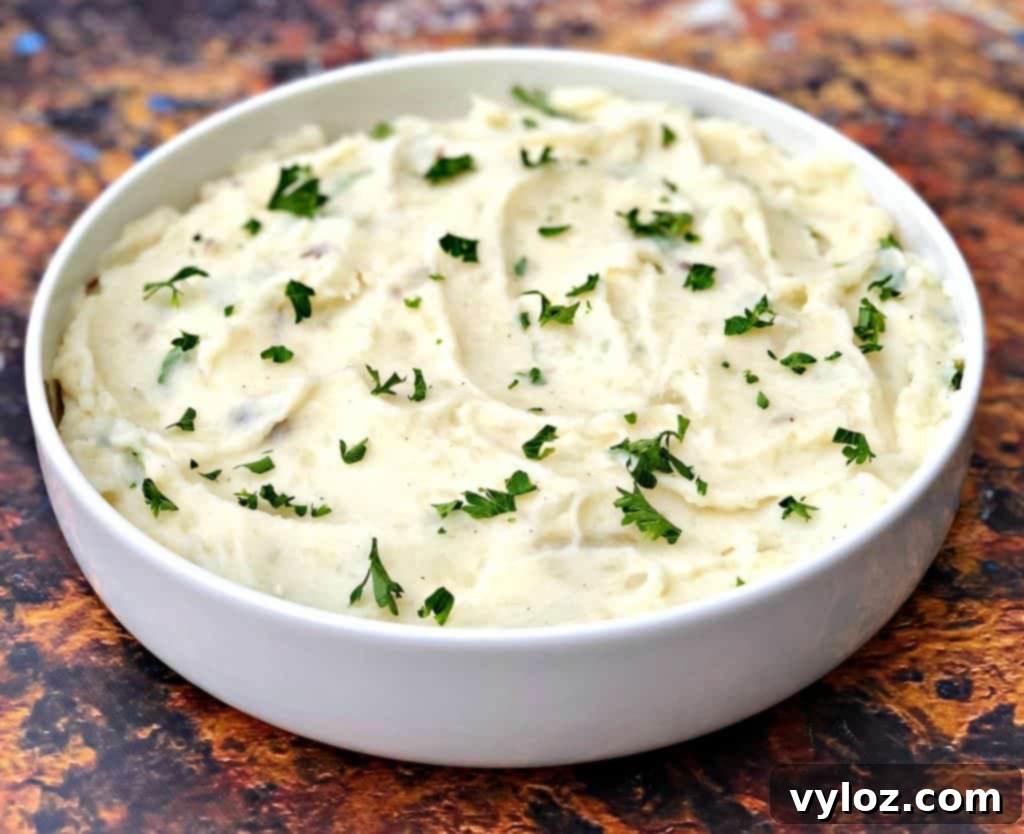 A close-up of creamy Instant Pot garlic mashed potatoes in a white bowl, garnished with fresh herbs.