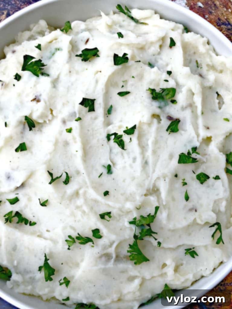 Close-up of a spoonful of creamy Instant Pot mashed potatoes being served from a large bowl, with more bowls in the background.