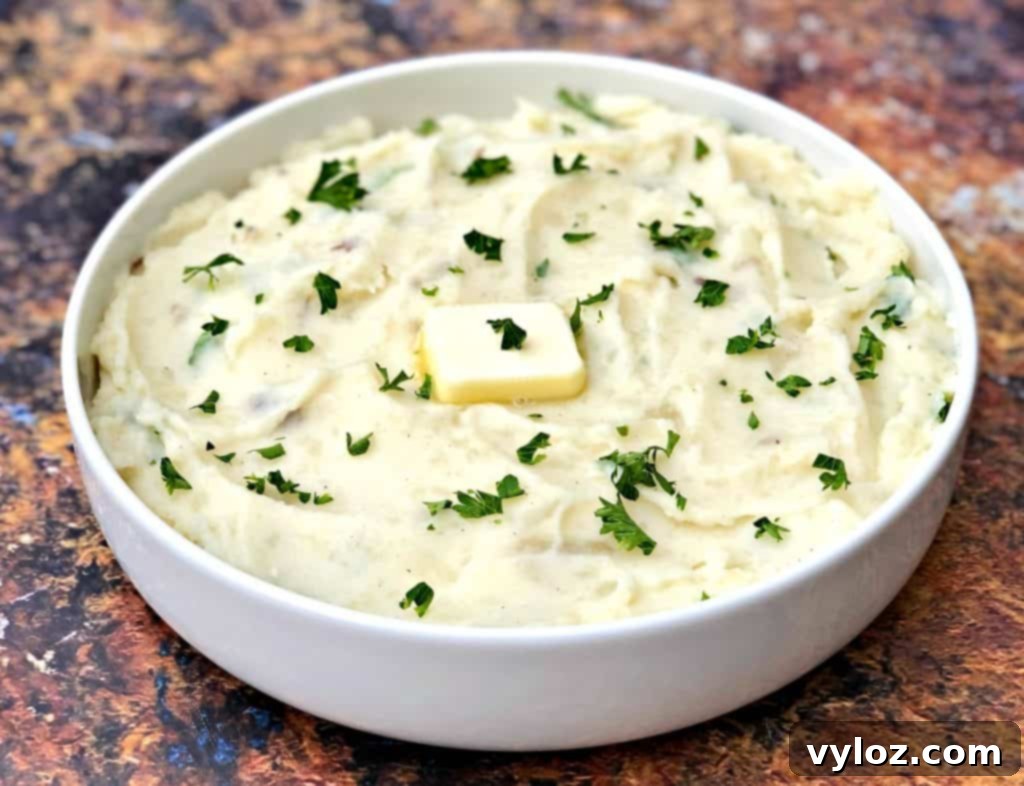 A single white bowl filled with creamy Instant Pot garlic mashed potatoes, set against a blurred background of a kitchen counter.