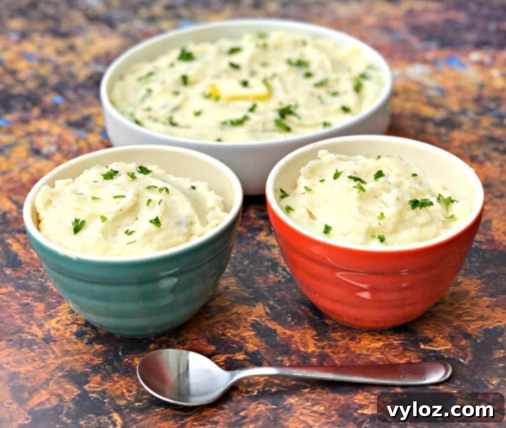 Three serving bowls overflowing with creamy Instant Pot garlic mashed potatoes, garnished with fresh herbs.