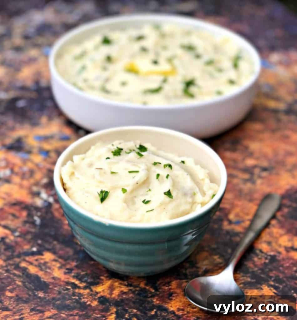 Two bowls of Instant Pot garlic mashed potatoes, one with a scoop and the other garnished, showcasing the creamy texture.