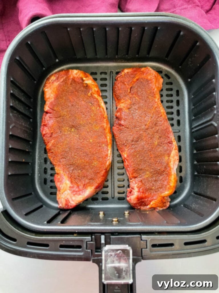 Close-up of raw seasoned steaks arranged in an air fryer basket before cooking.