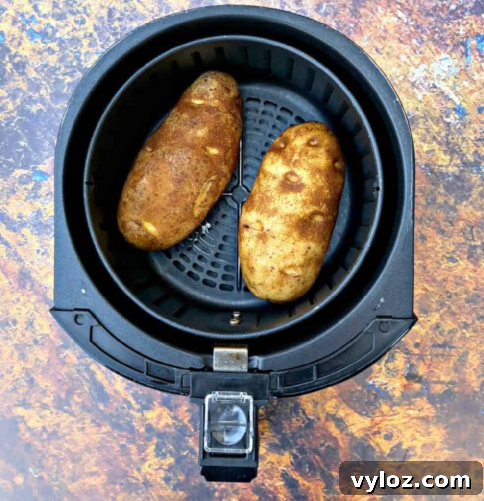 Crispy Air Fryer Baked Potatoes 4 Russet potatoes seasoned with oil and salt, placed in an air fryer basket, ready for cooking.