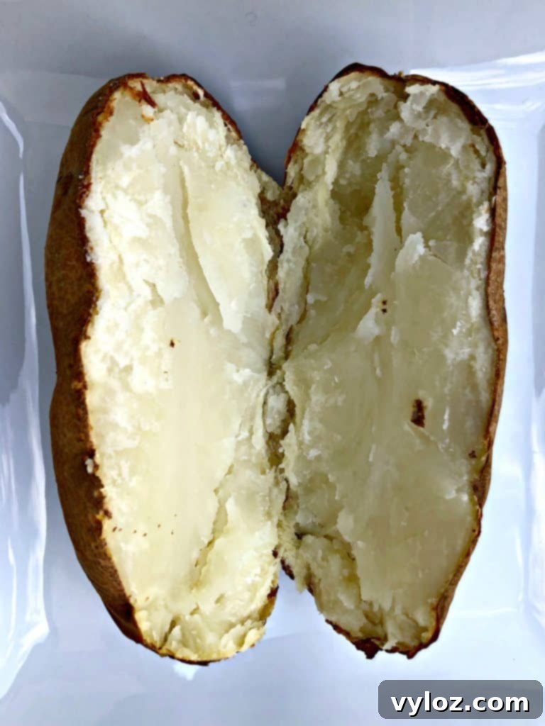 Crispy Air Fryer Baked Potatoes 5 A perfectly baked potato sliced in half on a white plate, revealing its fluffy interior, ready for toppings.