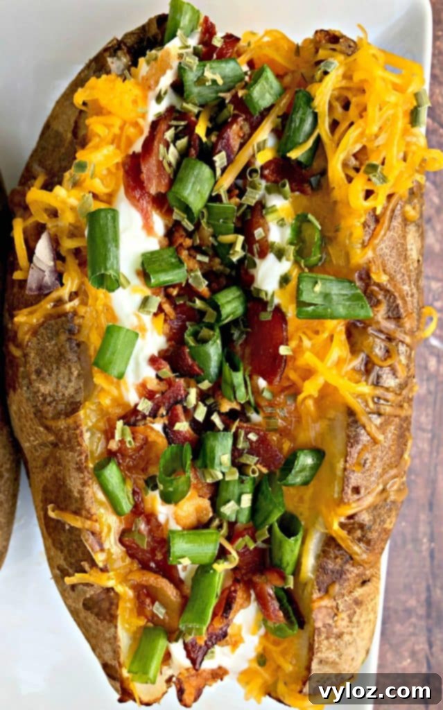 Crispy Air Fryer Baked Potatoes 8 A single loaded air fryer baked potato on a white plate, showcasing its golden-crisp skin and vibrant toppings.