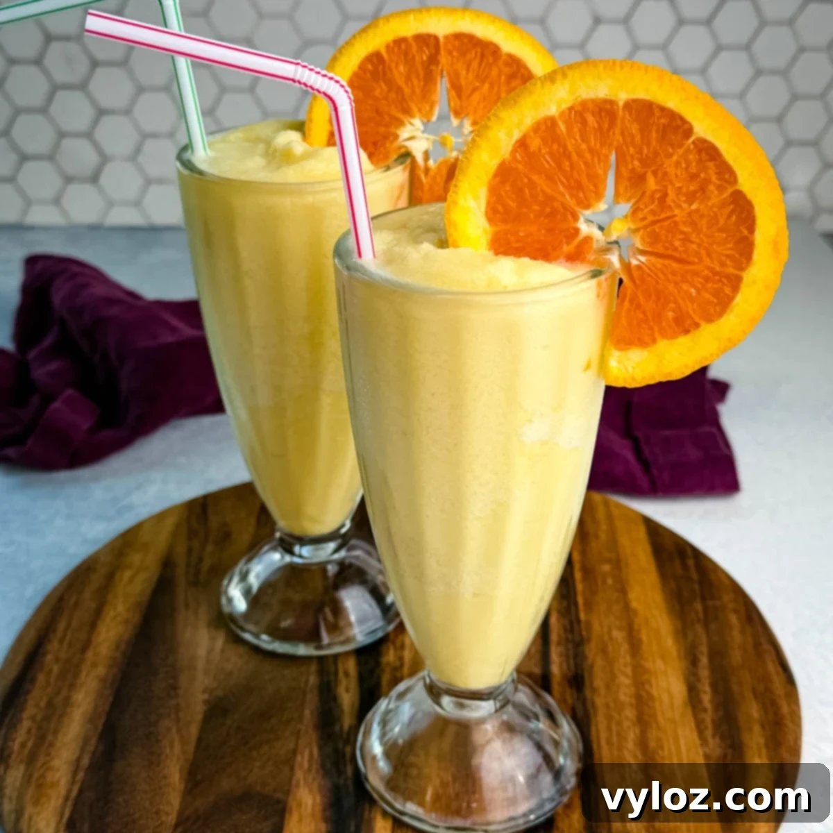 Two tall glasses filled with orange Julius slushies, garnished with orange slices and straws