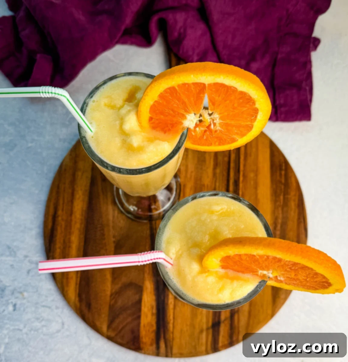 Two glasses of frozen orange Julius slush topped with orange slices and straws