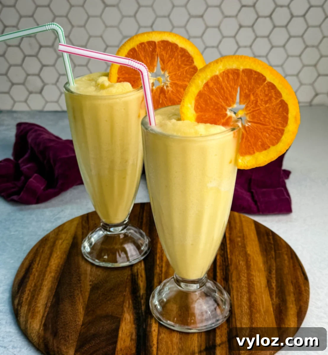 Two tall glasses of orange Julius slushies with orange slices and straws