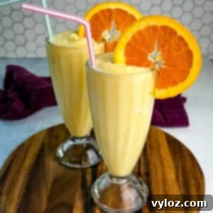 Two tall glasses filled with orange Julius slushies, garnished with orange slices and straws.